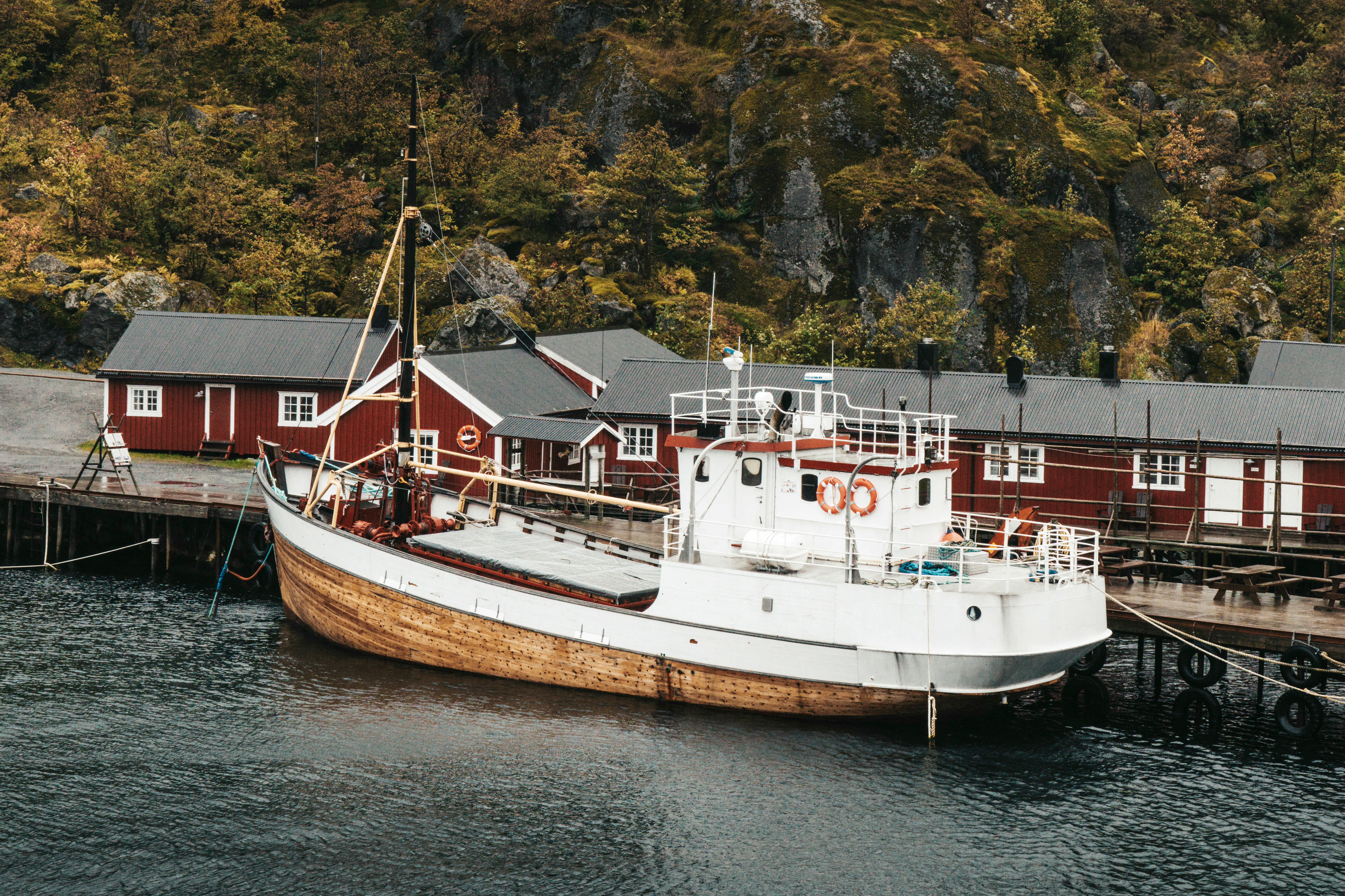 A traditional fishing boat docked at a quaint Nordic harbor surrounded by lush greenery.
