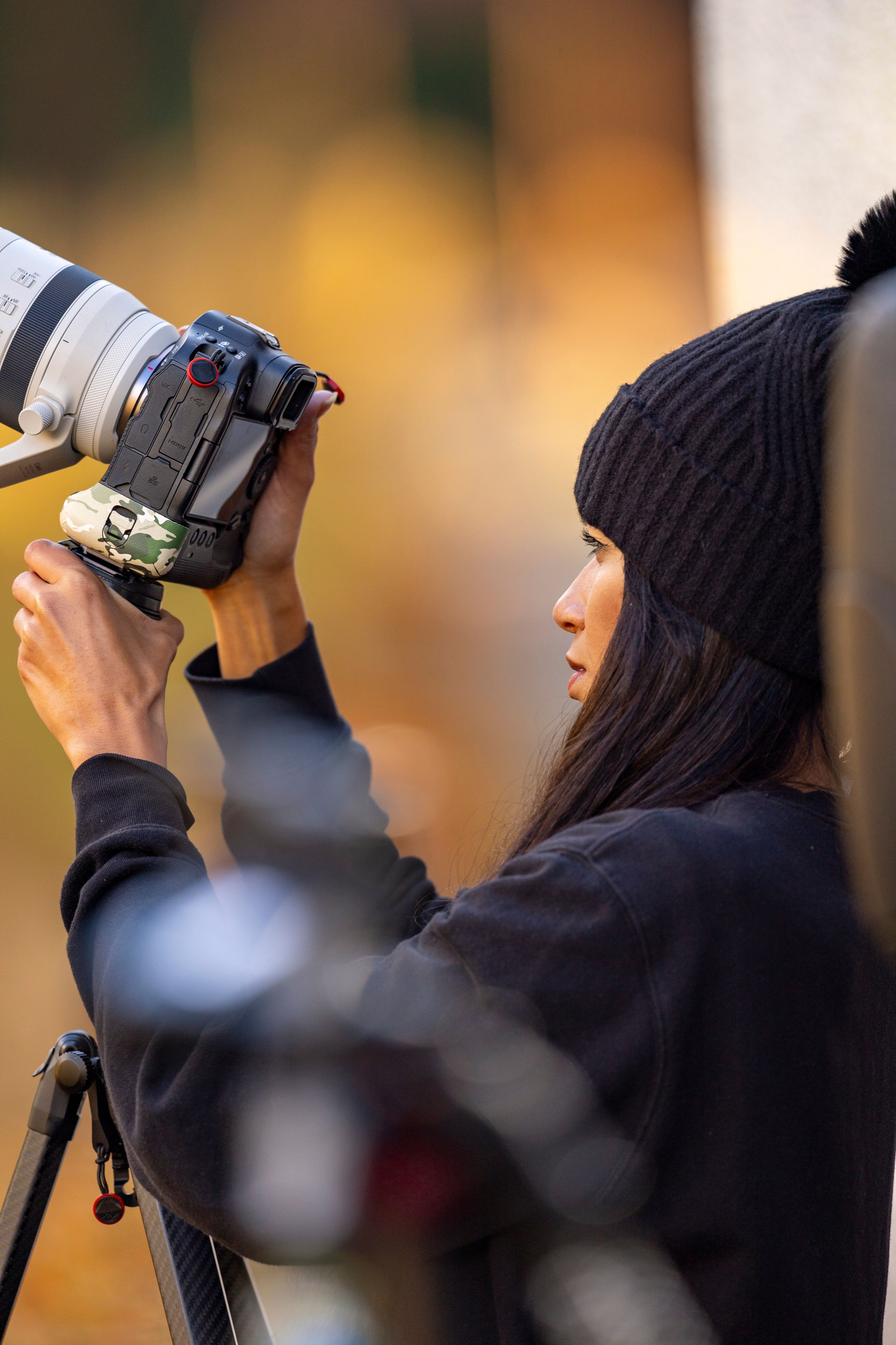 Female photographer with long lens adjusting settings during fall season.