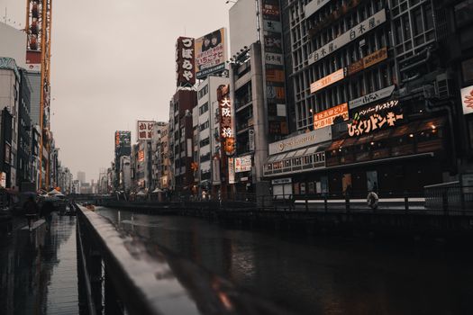 Moody street view of Dotonbori in Osaka on a rainy day with neon signs reflecting in the water.