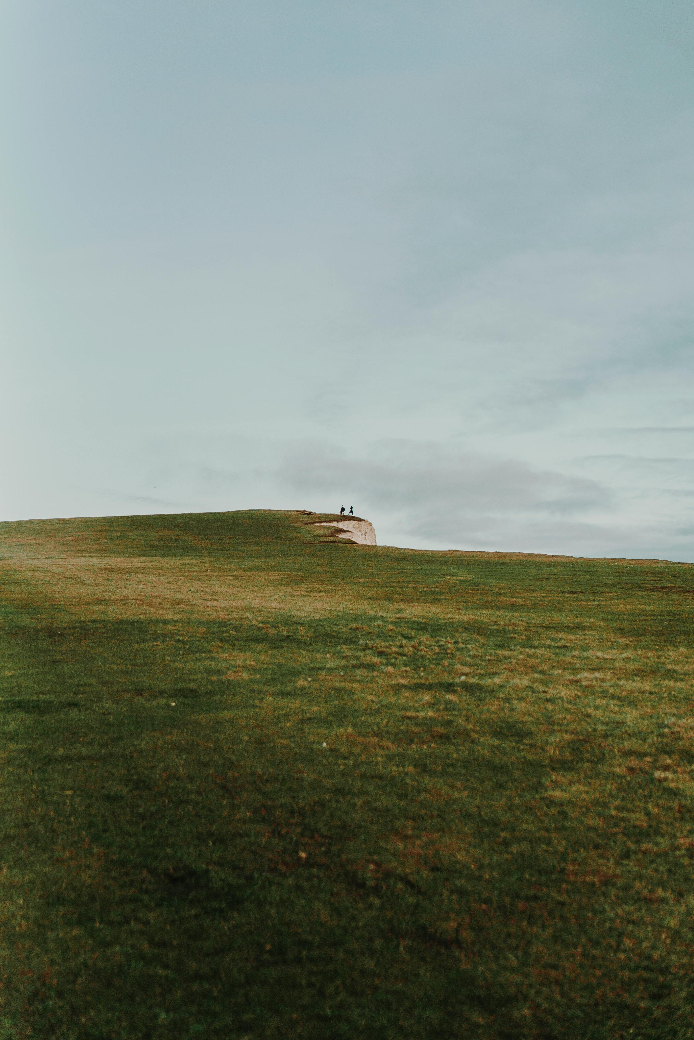 在广阔的天空下，一座长满草的小山通向悬崖边缘，构成一幅广角照片