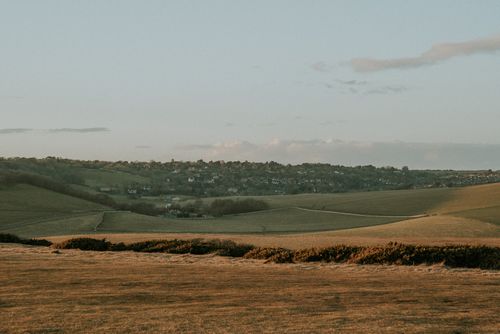 Free A peaceful view of rolling hills and a town under a soft sunset sky. Stock Photo