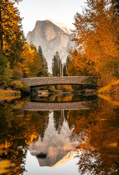 Free Tranquil autumn scene of a stone bridge and Half Dome in Yosemite, mirrored in still waters. Stock Photo