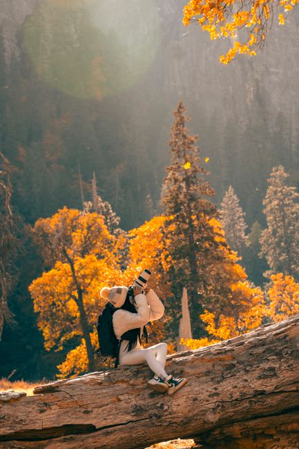 A person wearing cozy attire captures stunning autumn scenery in a forest.