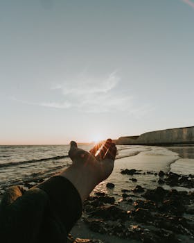 Hand reaches towards a serene ocean horizon at sunset, capturing peaceful nature vibes.