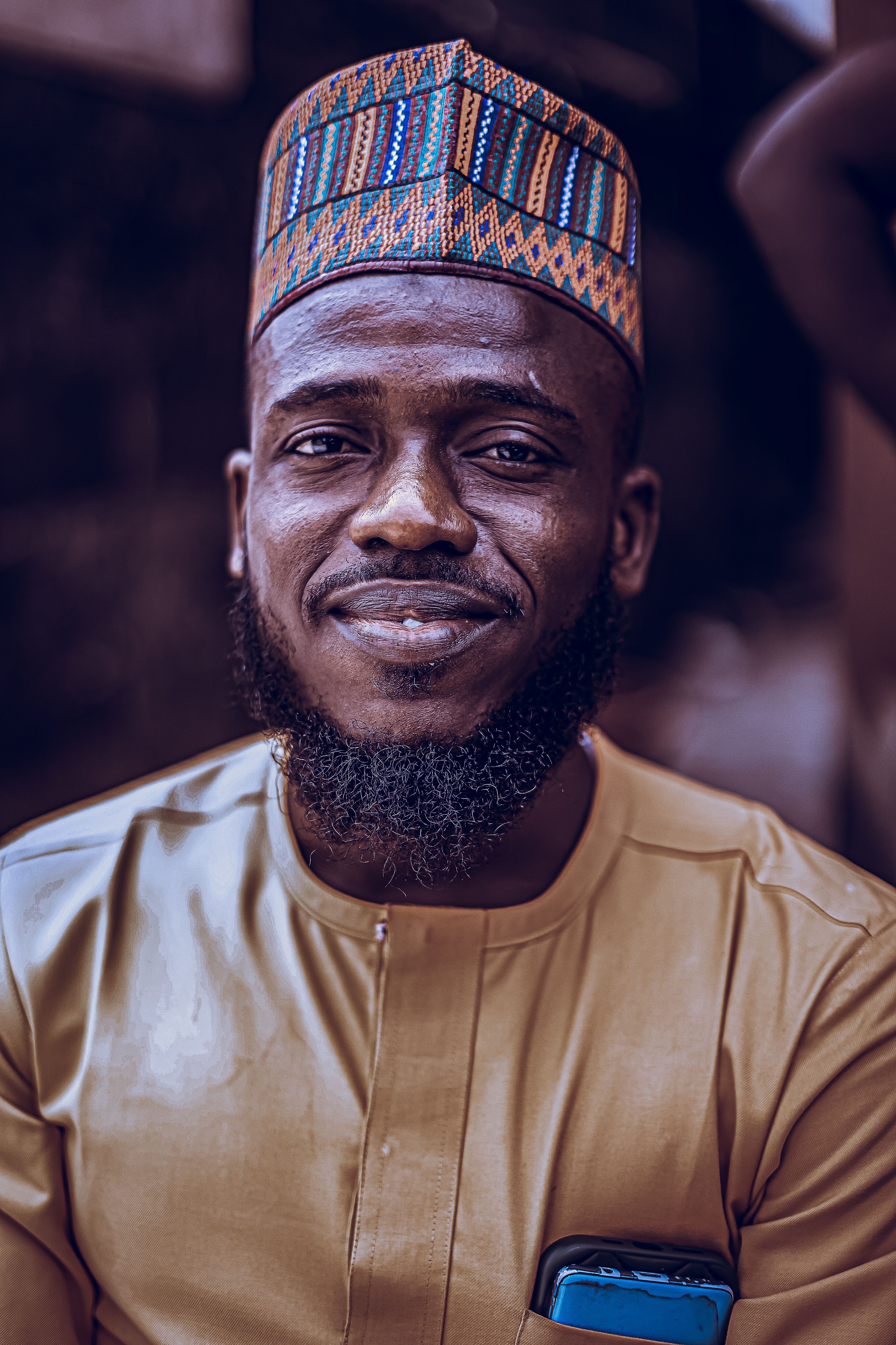 Close-up portrait of a man in traditional African dress, smiling warmly outdoors.