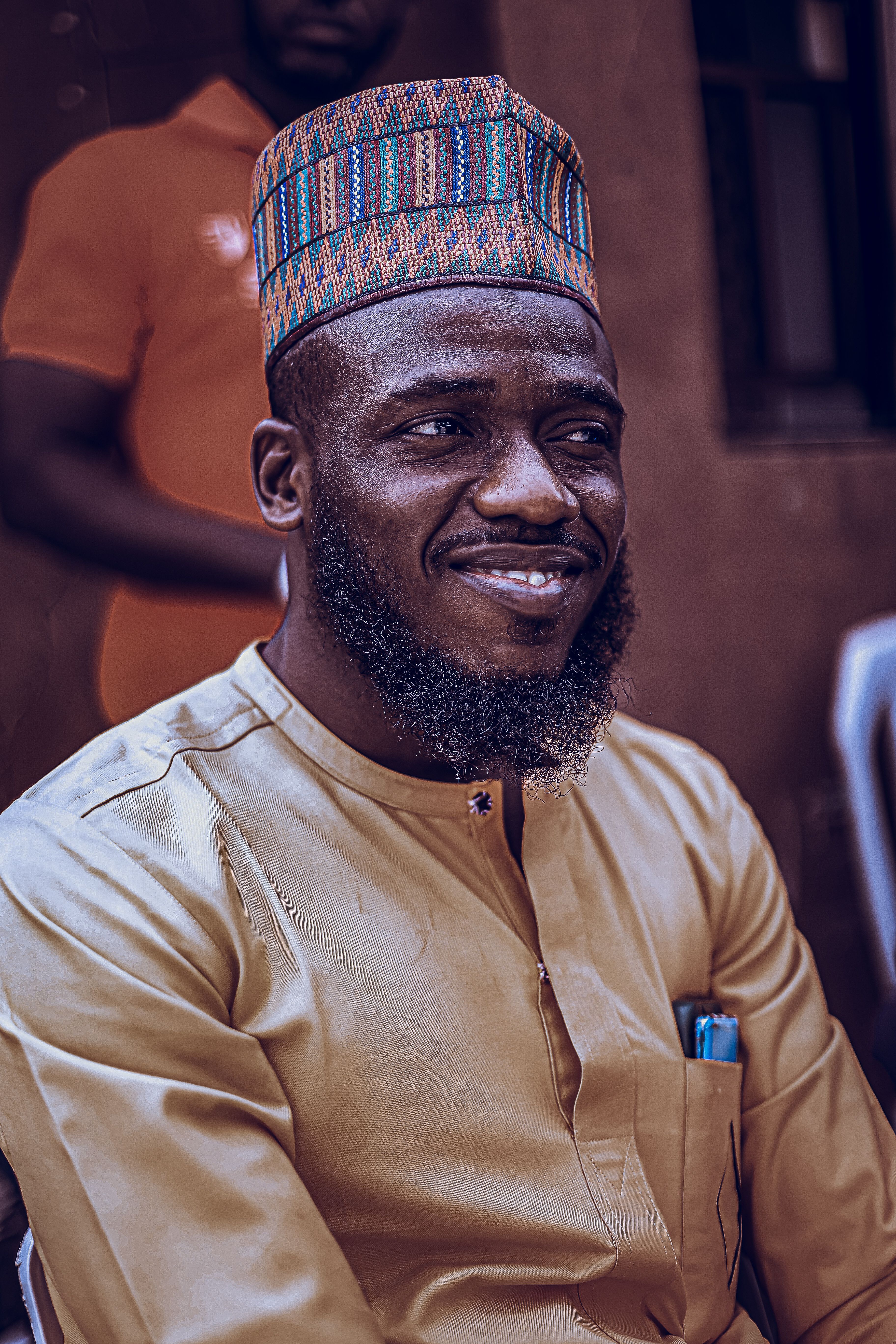Man wearing traditional African attire with a patterned hat, smiling warmly.