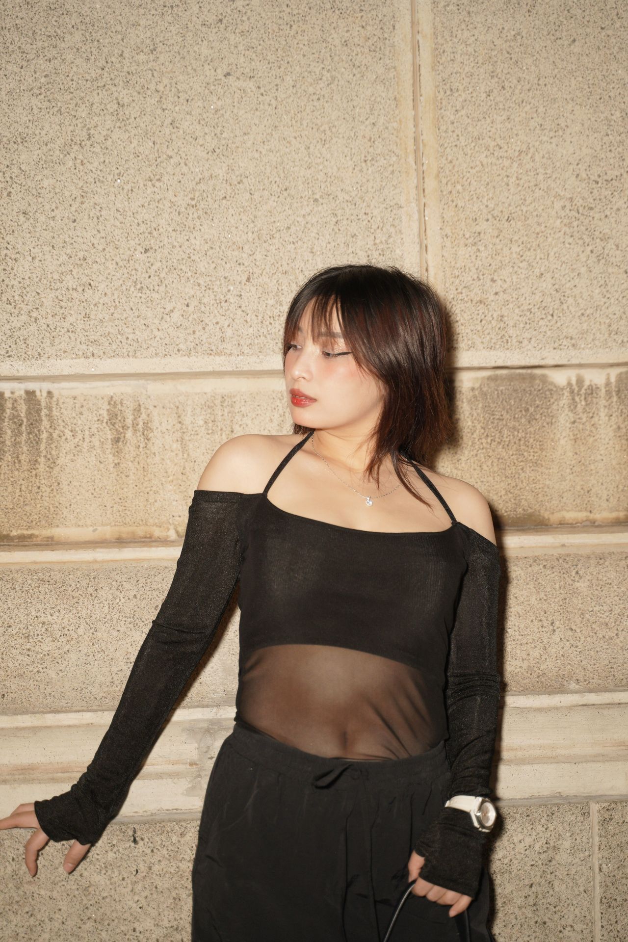 Woman in a black mesh-panel long-sleeve top against a stone wall