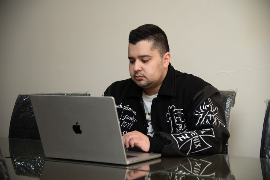 Man in black jacket working on a laptop indoors, showcasing modern technology use.
