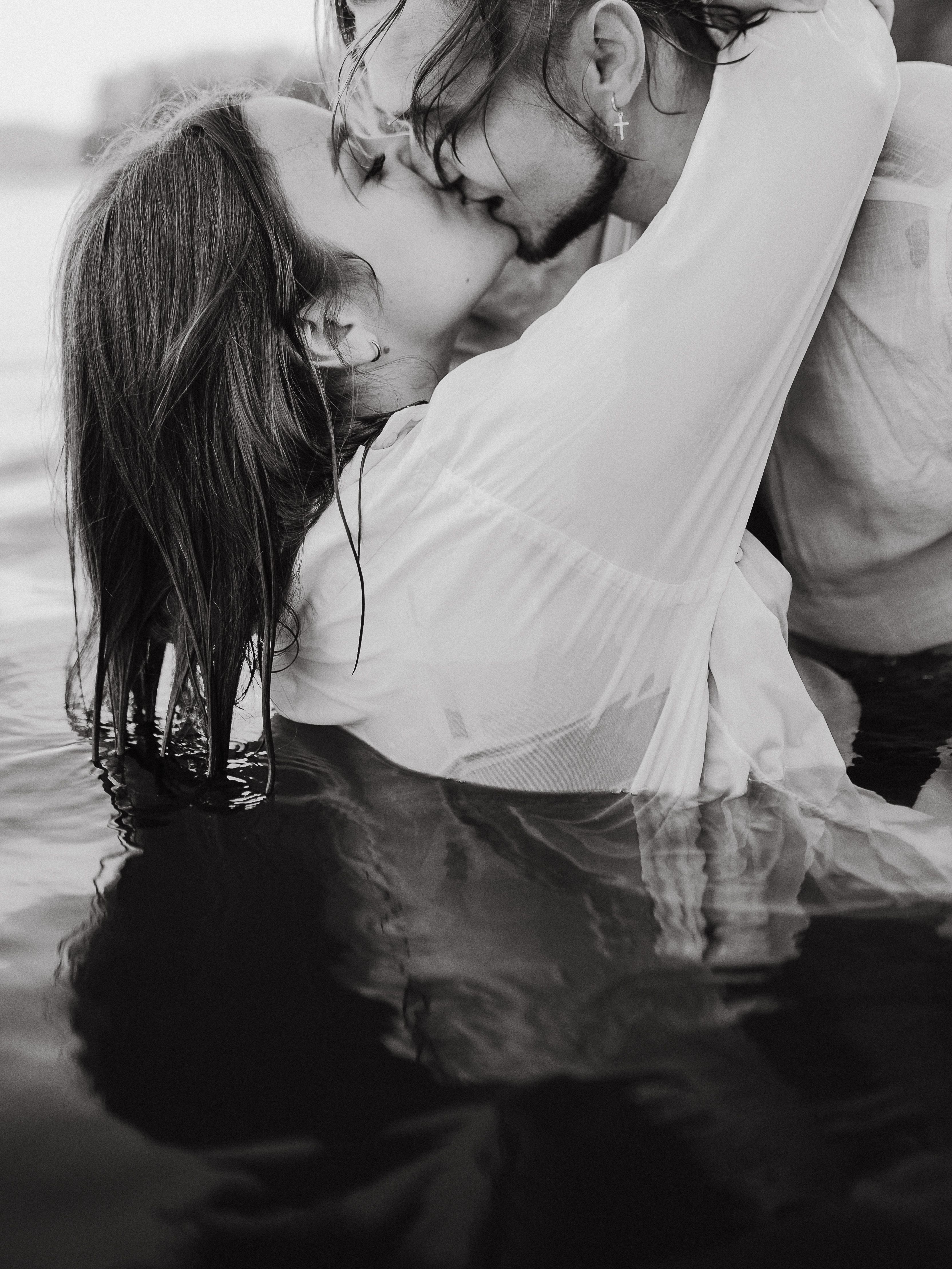 A romantic black and white photo of a couple kissing passionately in water.