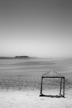 A tranquil black and white image of a deserted beach with a lone canopy and vast sky.