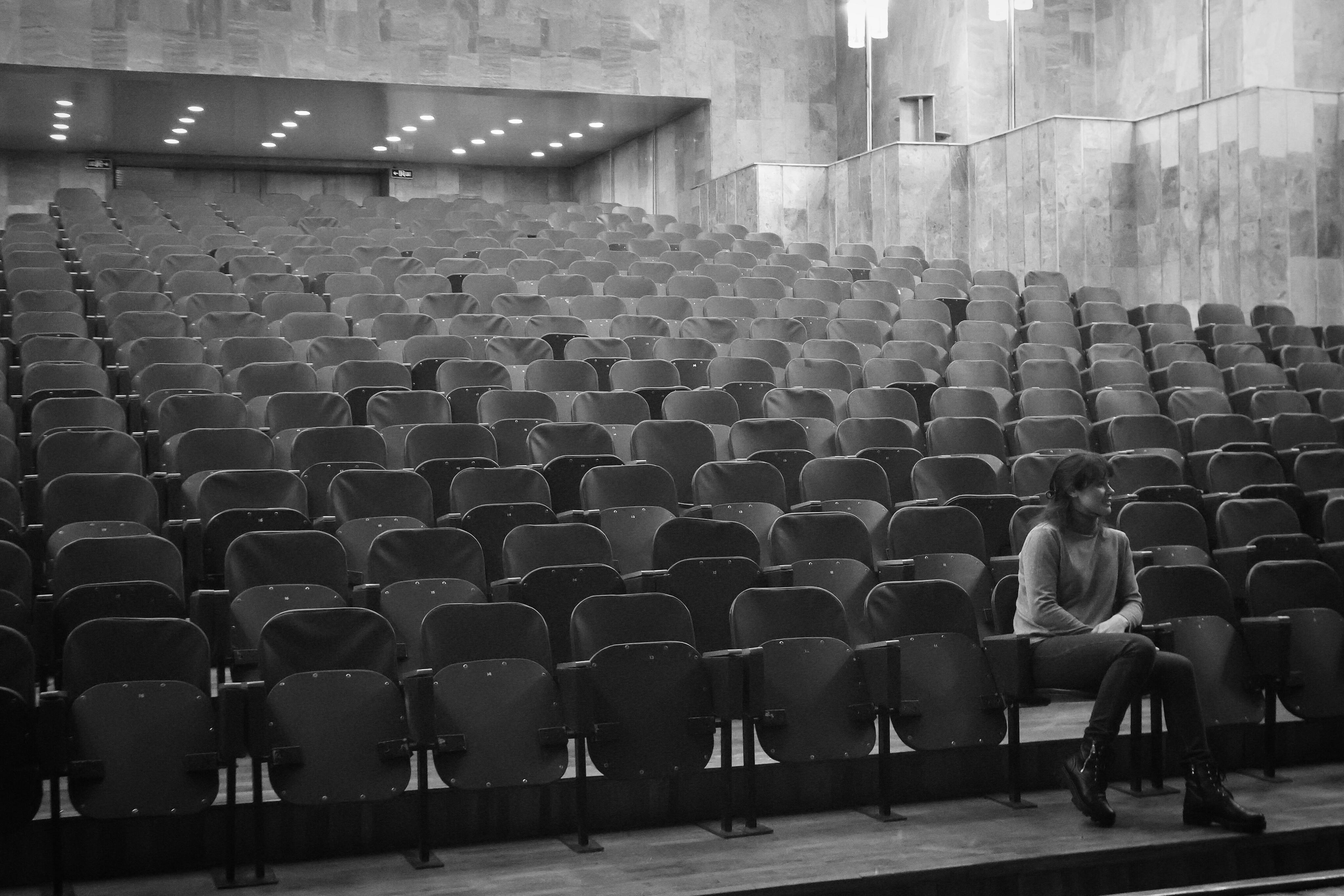 gratis Een eenzame vrouw zit in een groot leeg auditorium, wat een gevoel van eenzaamheid creëert. Stockfoto