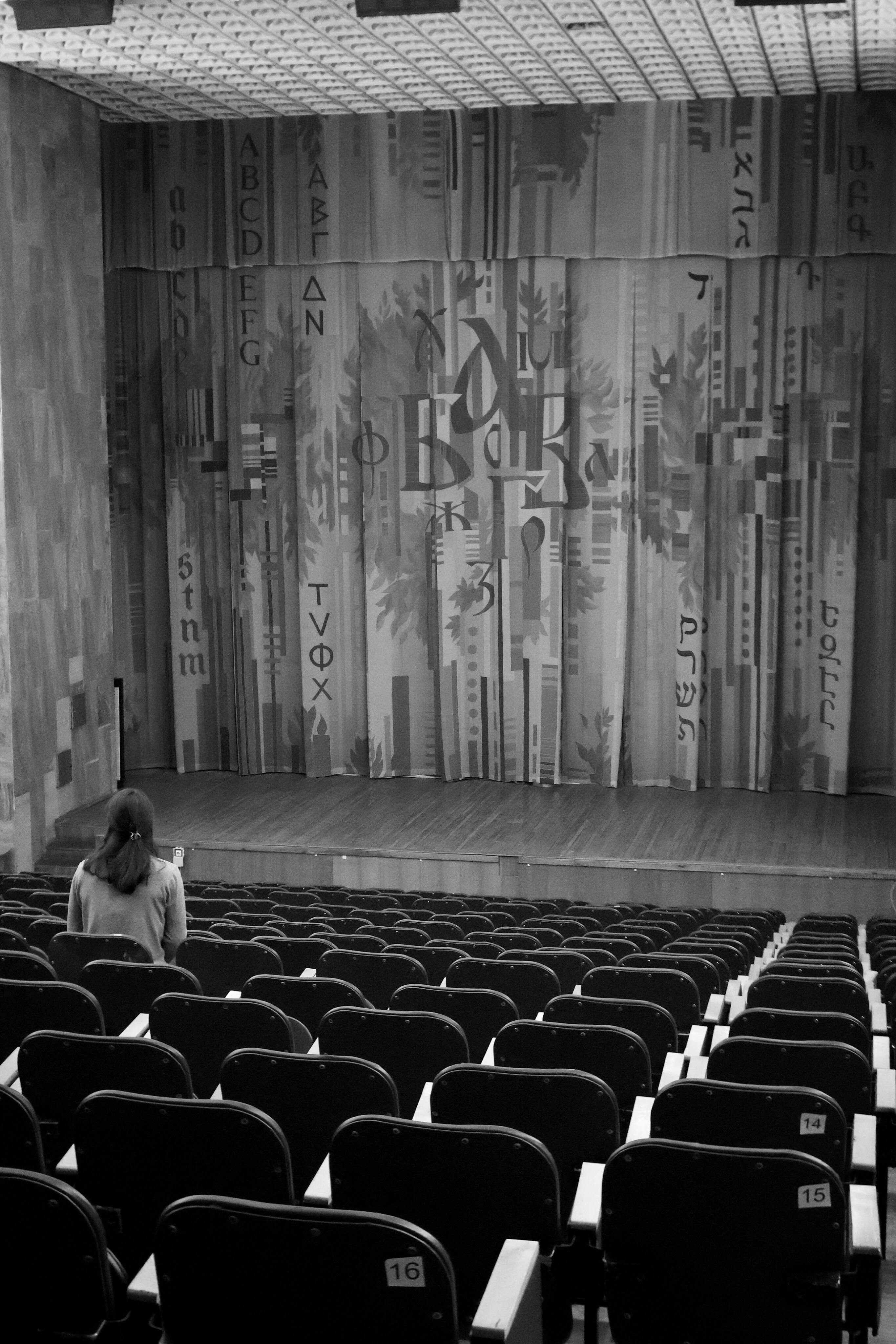 gratis Een eenzame persoon zit in een leeg theater met een artistiek gordijn op de achtergrond. Stockfoto
