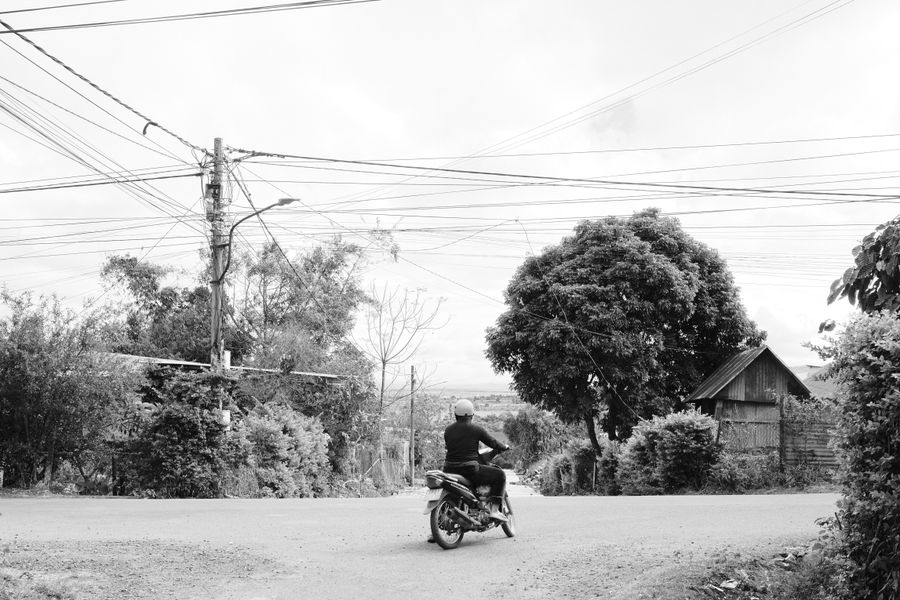 Black and white photo of a motorcyclist at a crossroads in a rural area.