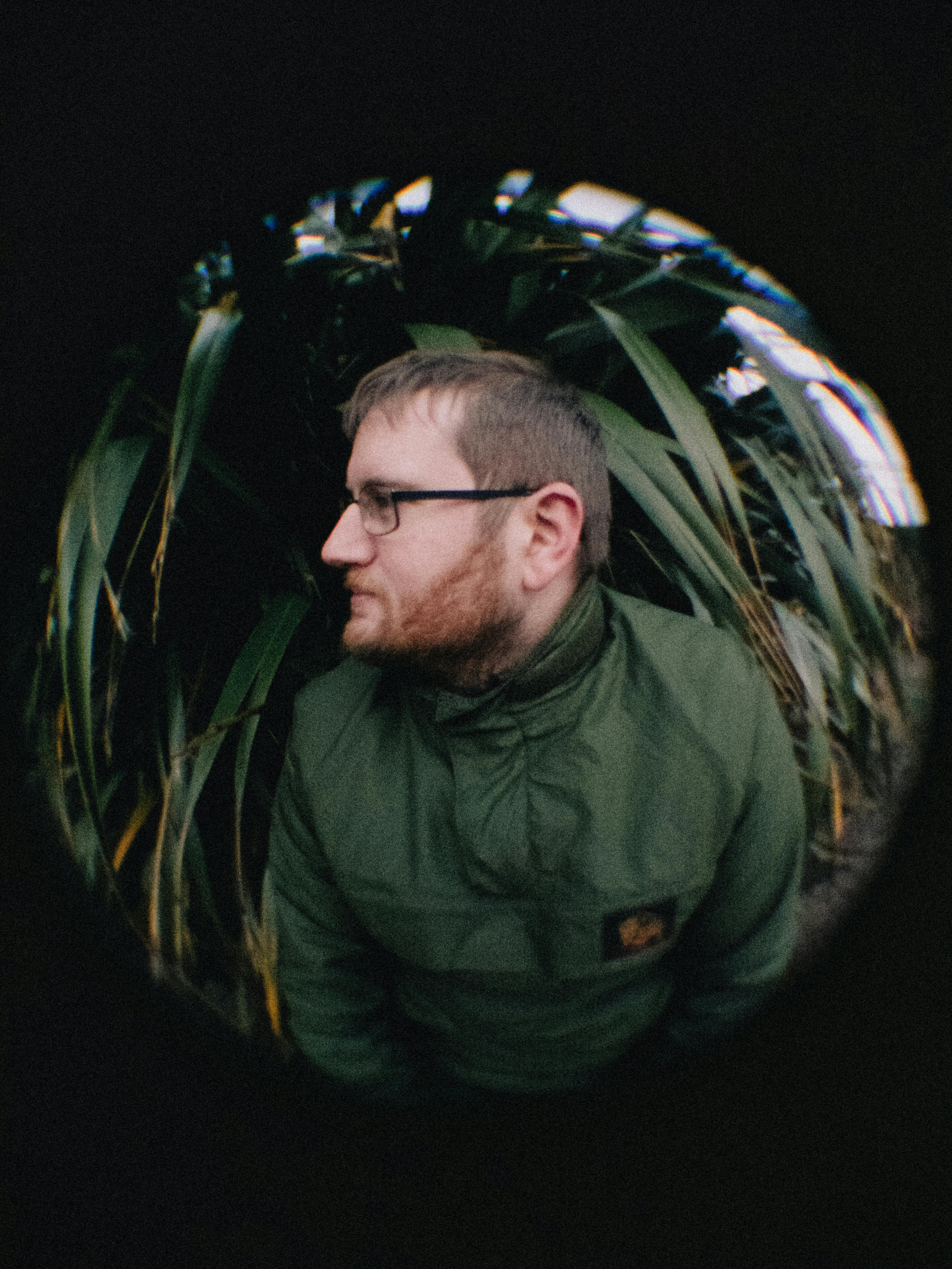 Profile of a man in a green jacket captured with a fisheye lens against foliage background.