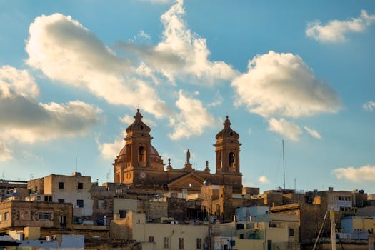 A scenic view of a Maltese basilica against a backdrop of scattered clouds in a blue sky.