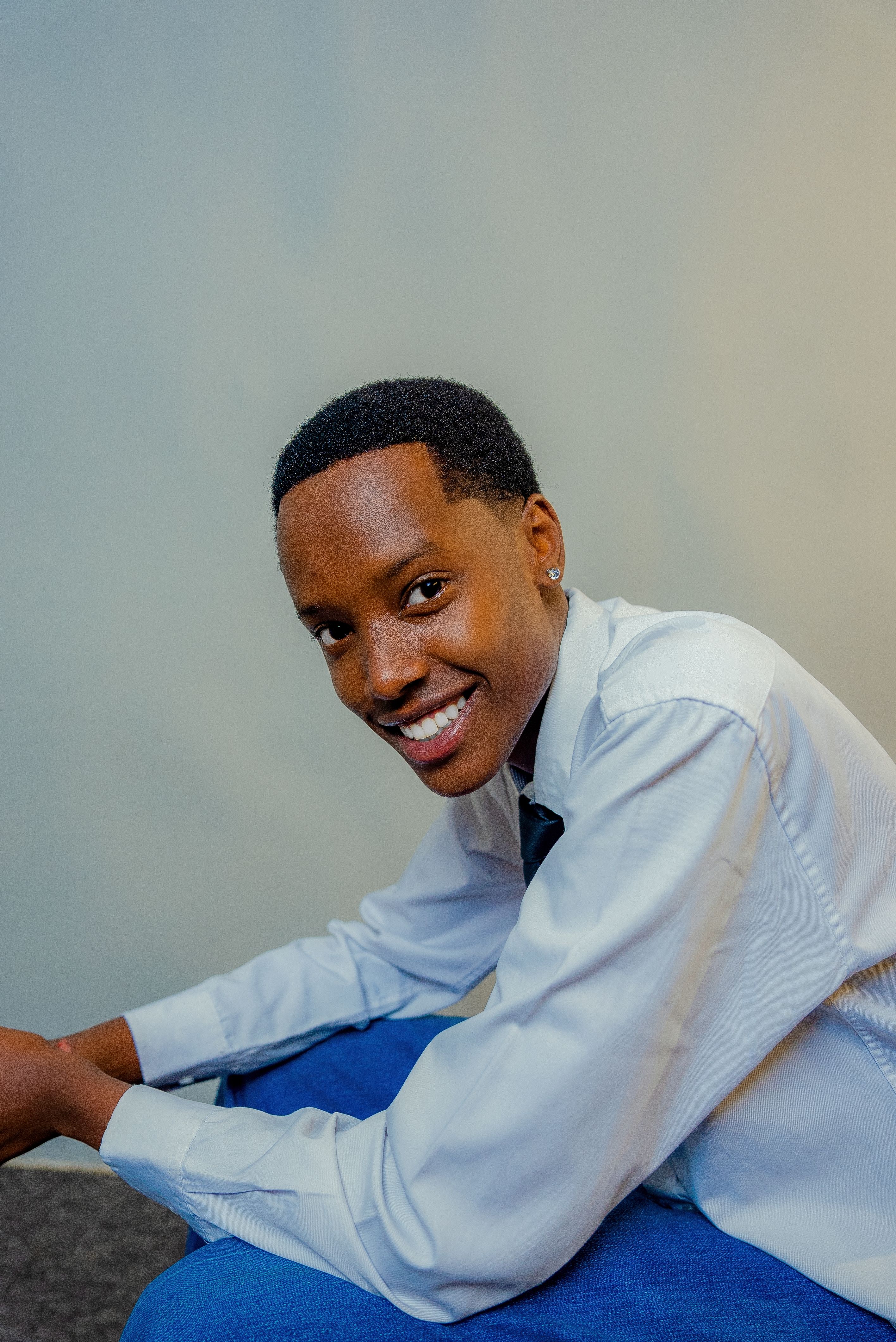 Portrait of a smiling young adult wearing a white shirt and blue pants indoors.