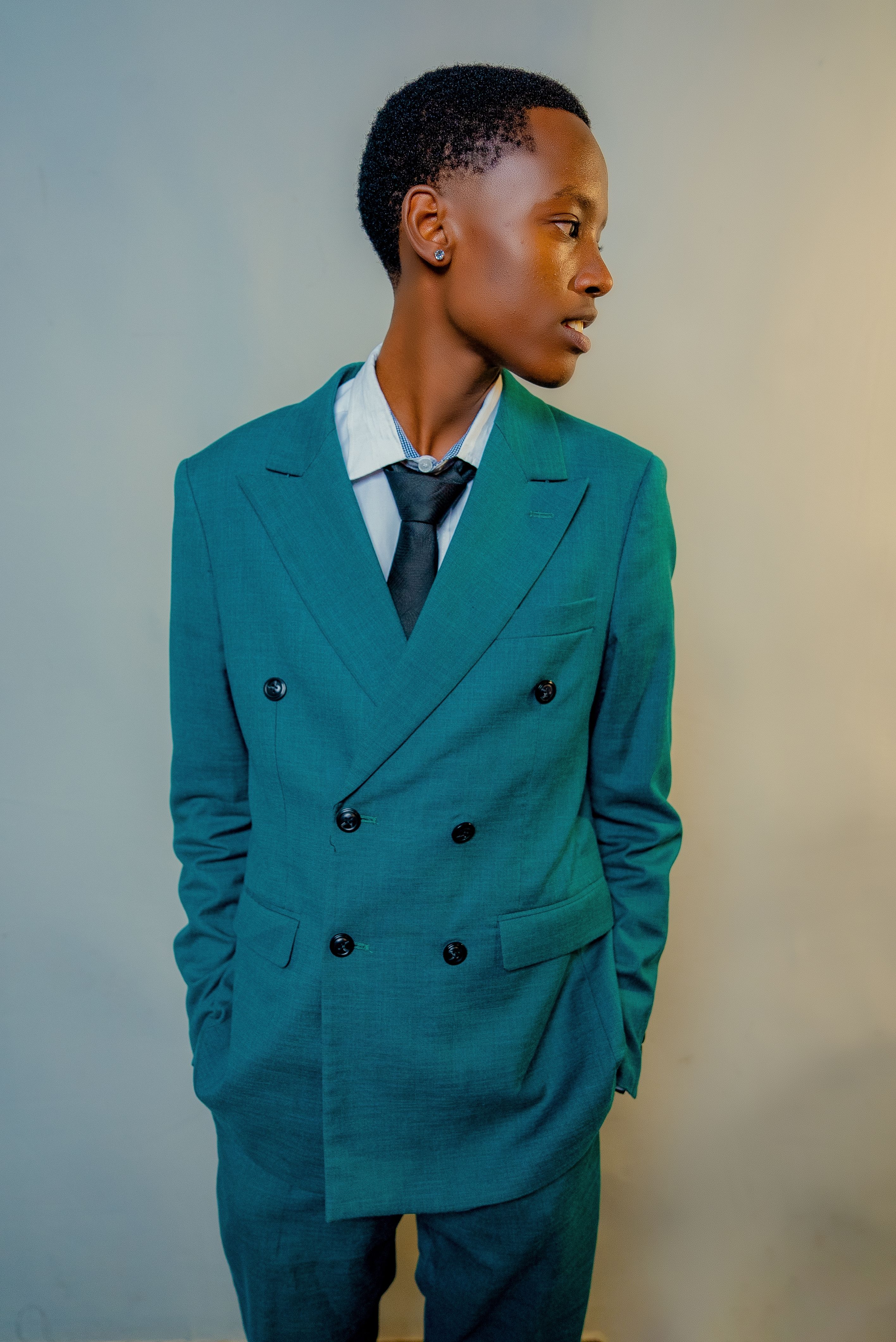 Elegant portrait of a person in a teal suit with a black tie, displaying modern fashion.