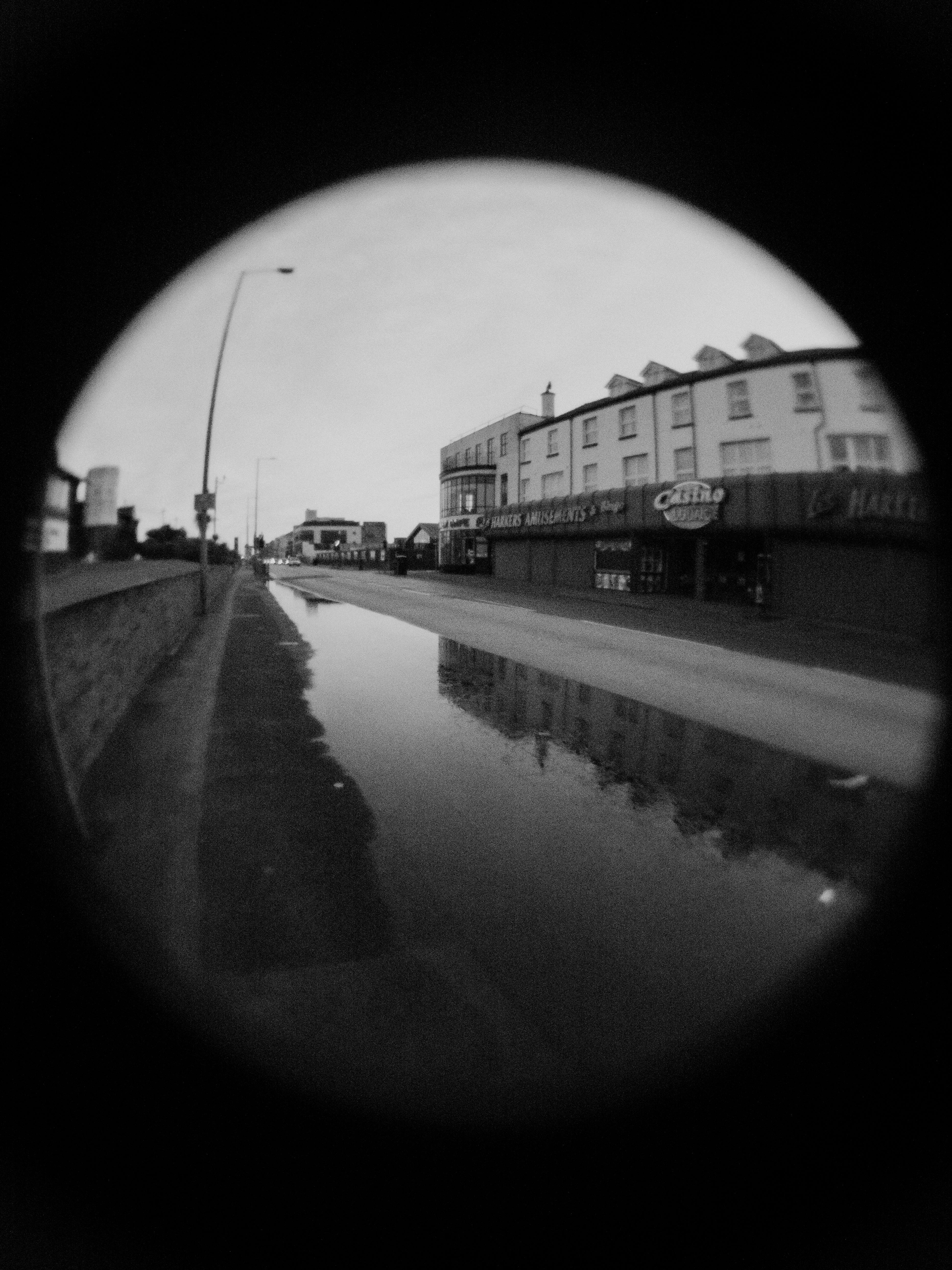 A moody urban street scene captured through a fisheye lens in black and white.