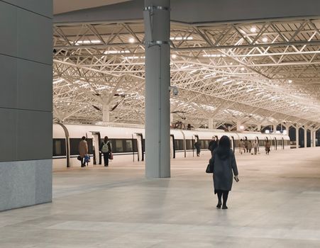 A modern train station interior with passengers walking towards a waiting train.