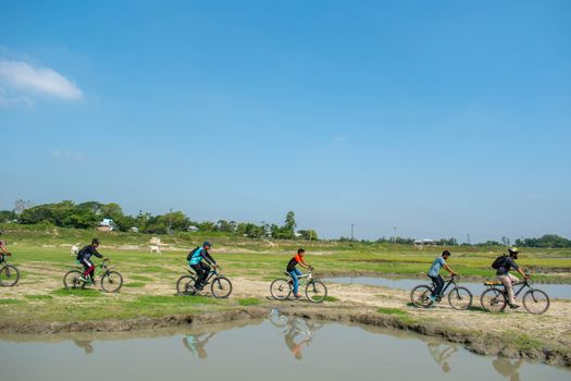A group of cyclists riding through a scenic landscape with greenery and blue sky.