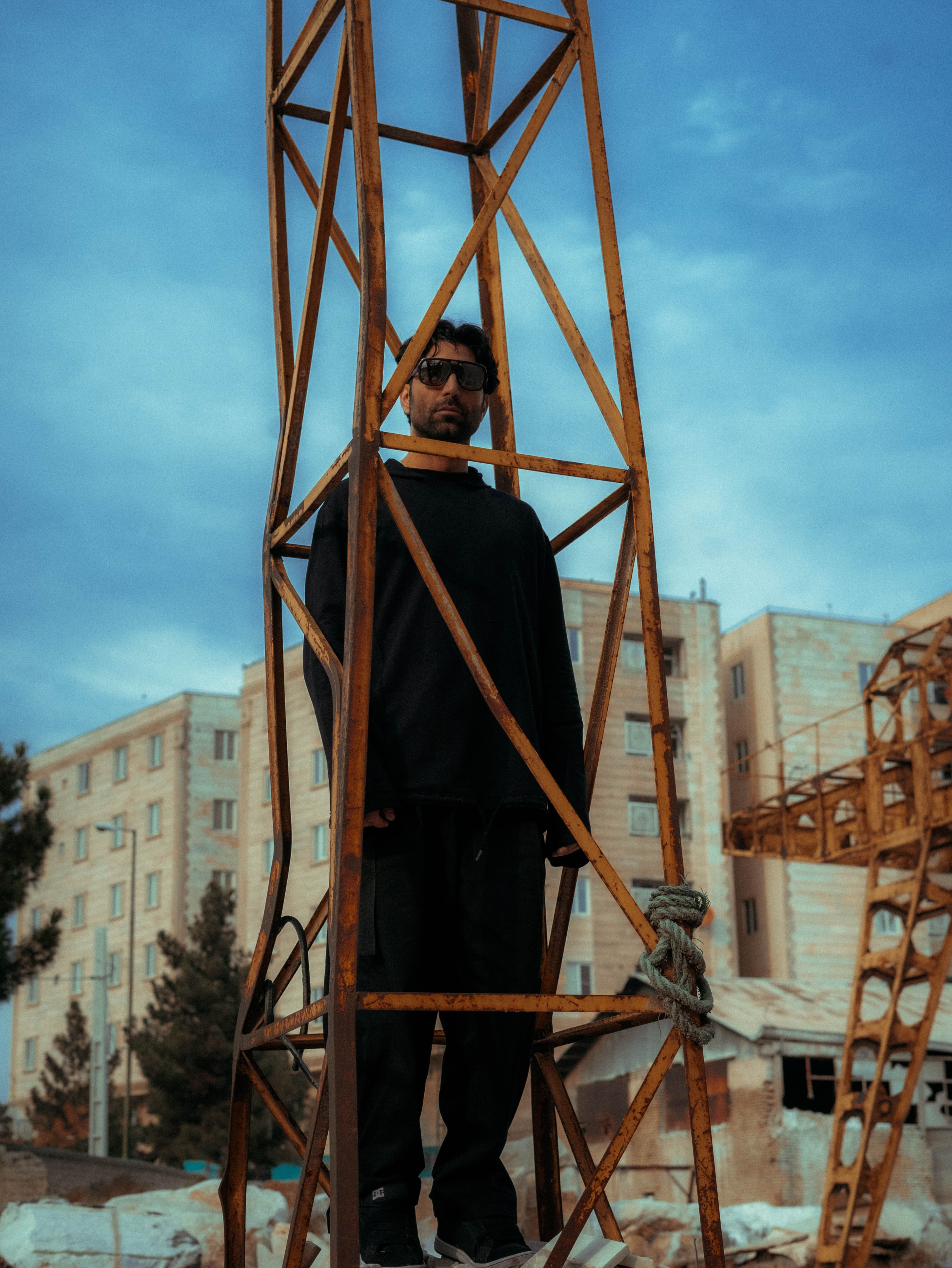 Man standing within an industrial framework against an urban backdrop.