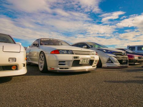 A lineup of classic JDM cars featuring a Nissan Skyline R32 at an outdoor car meet.