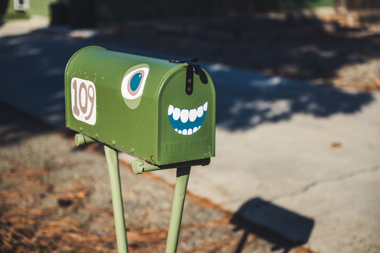 a fun and quirky green mailbox with a cartoon face on a sunny street i