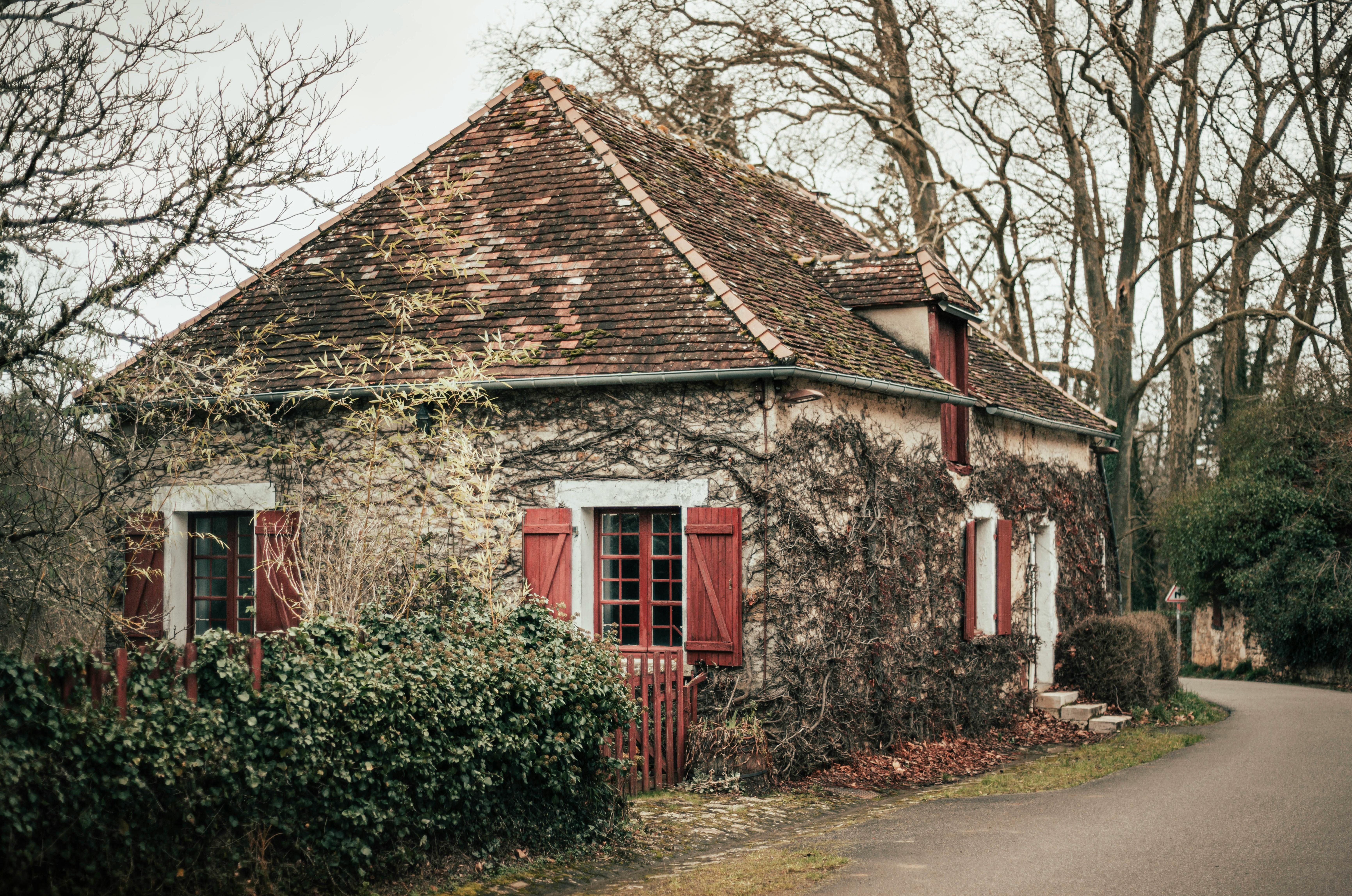 Picturesque rustic cottage with red shutters and ivy-covered walls in rural France.