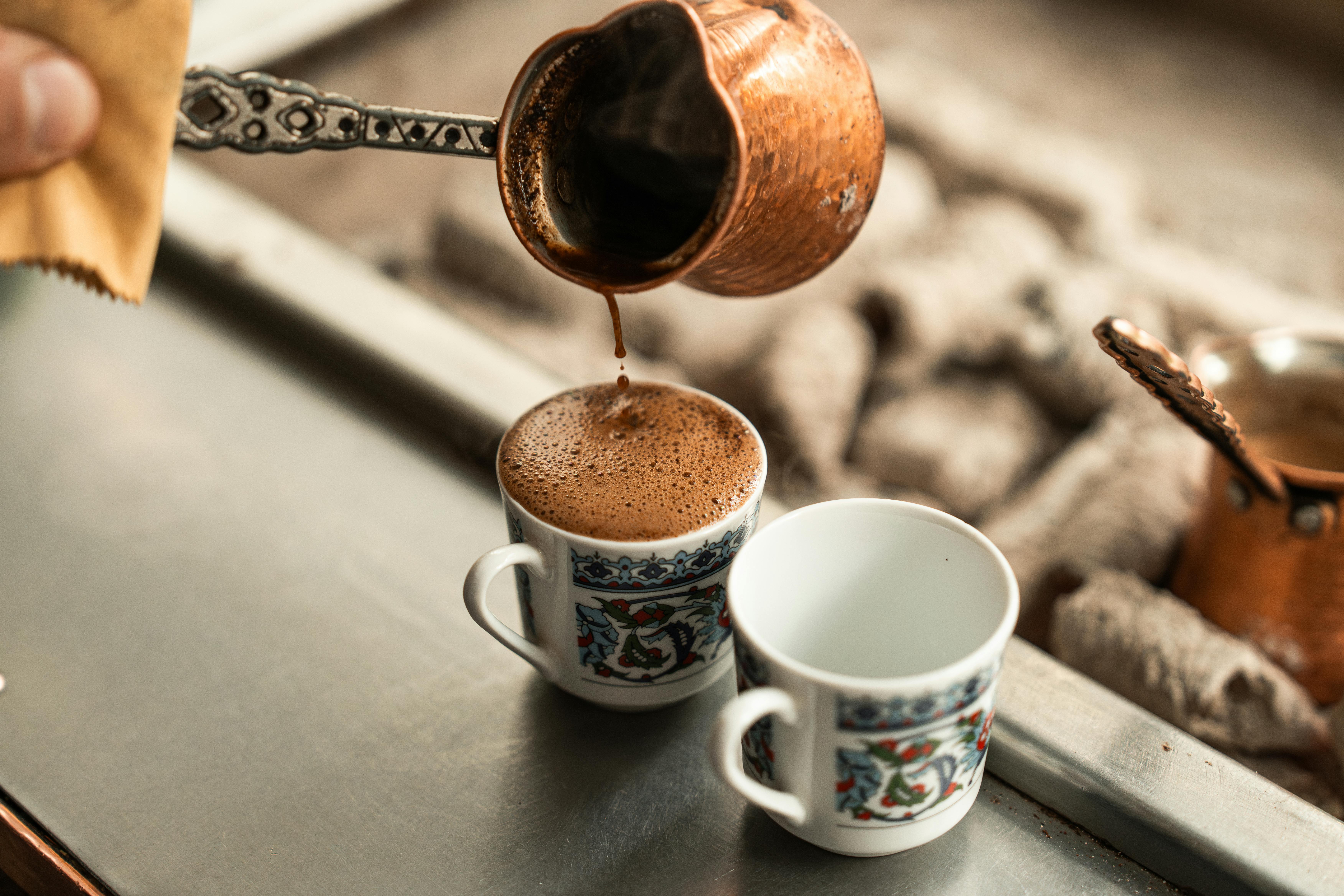 Close-up of Turkish coffee being freshly poured into ornate cups from a copper cezve.