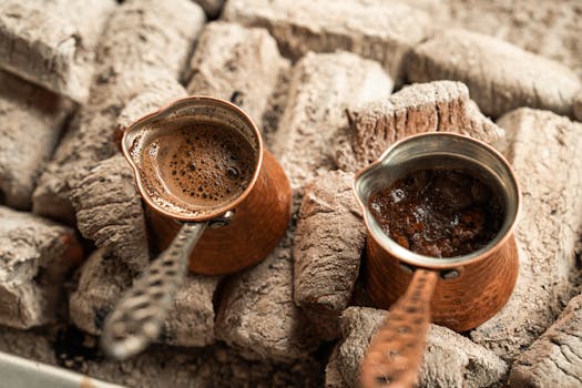 Two copper pots of Turkish coffee brewing on hot coals, capturing a rustic and authentic experience.