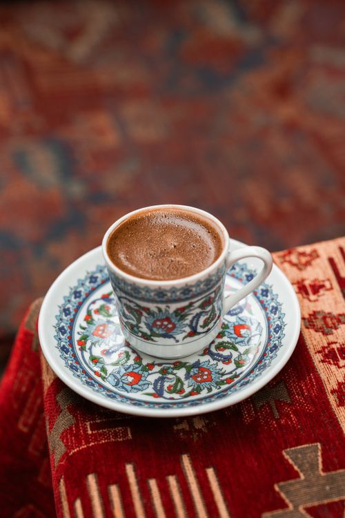 Free A beautifully decorated cup of Turkish coffee sits on an intricate saucer atop a vibrant patterned fabric. Stock Photo