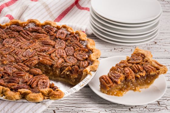 Pecan pie missing a wedge beside a plated slice and a stack of white plates