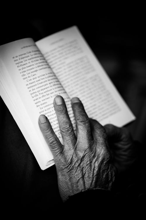 Free A black and white photo of an elderly hand holding an open book, conveying wisdom and experience. Stock Photo