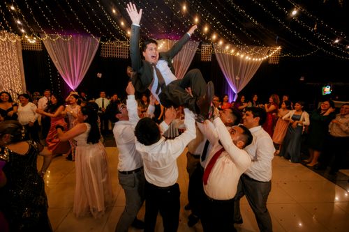 Free Guests celebrate joyfully at a wedding, lifting the groom amid laughter and dancing. Stock Photo