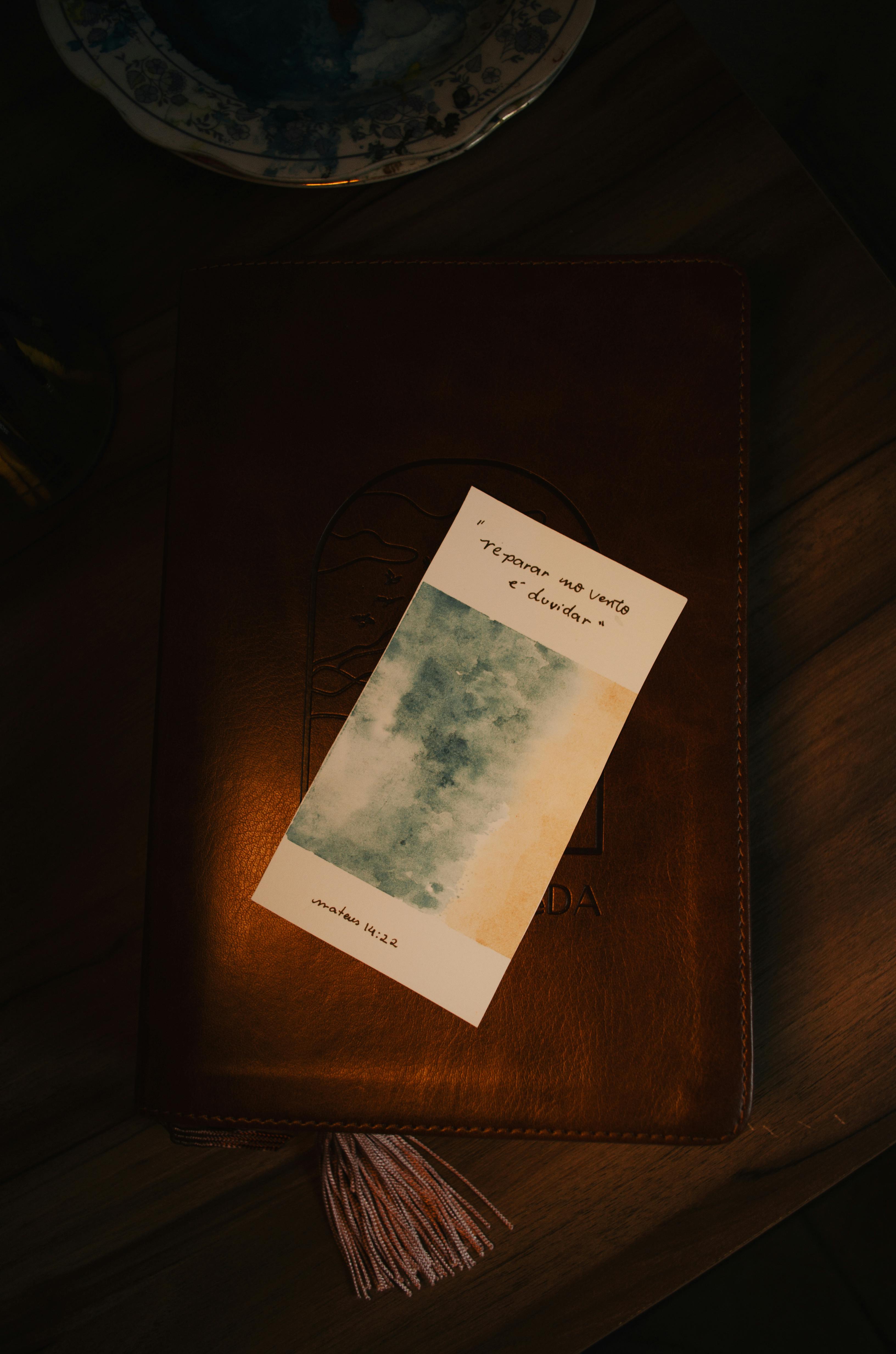 grátis Uma natureza morta com um cartão abstrato texturizado sobre um livro de couro, capturada em iluminação quente. Foto profissional