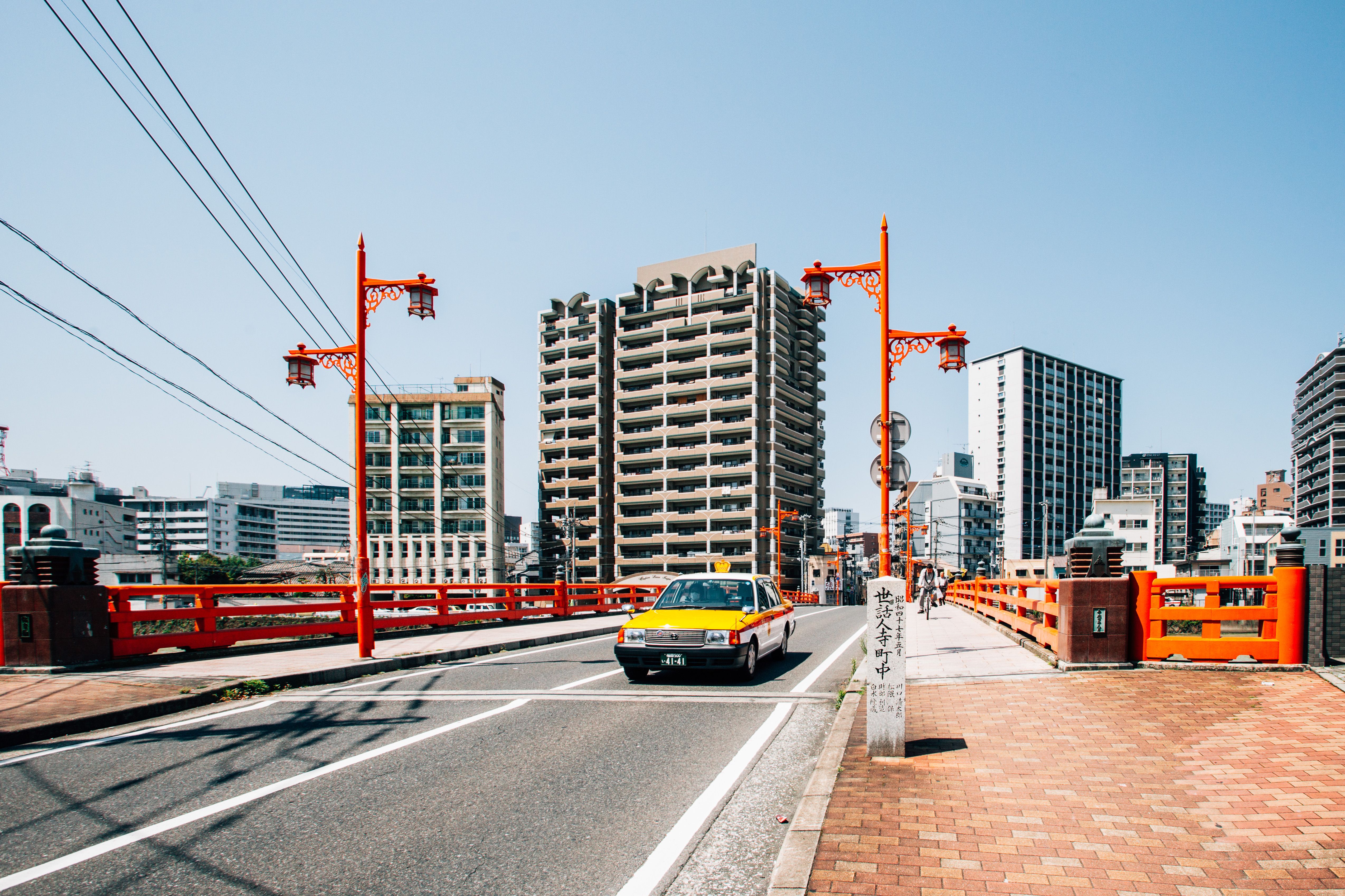 阳光明媚的日子里，充满活力的城市街景中，一座红桥位于前景，前方有一辆出租车