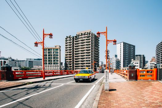 阳光明媚的日子里，充满活力的城市街景中，一座红桥位于前景，前方有一辆出租车