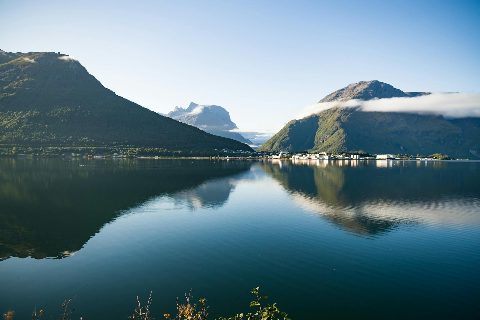 Peaceful landscape of Norwegian mountains reflected in a calm lake under clear skies.