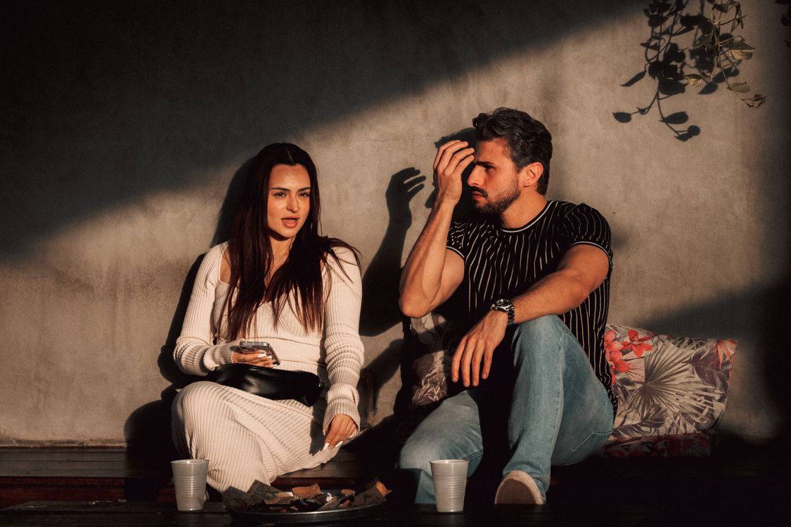 A man and woman sit outdoors and talk in natural light