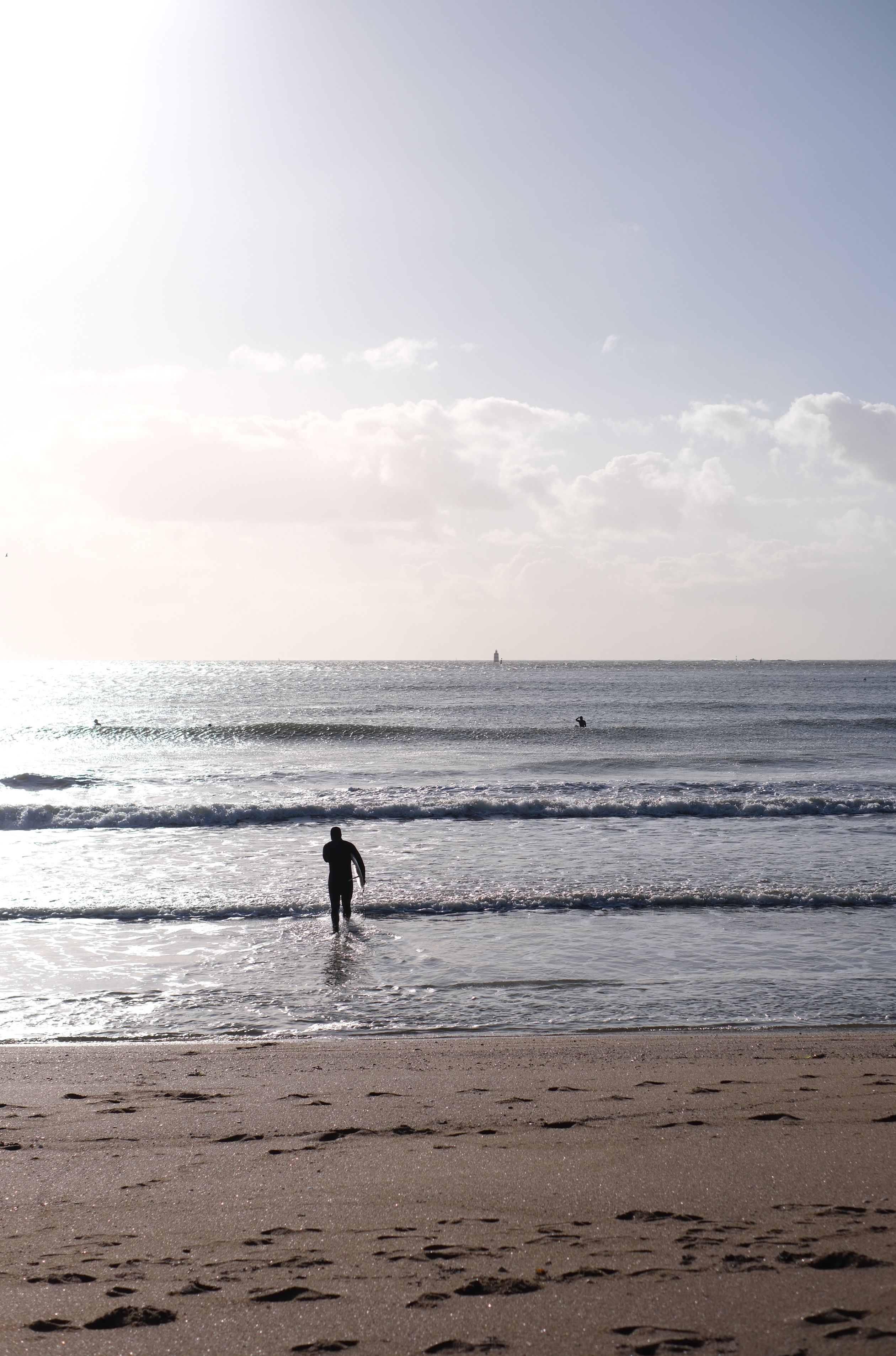 A lone figure walks into the ocean during a peaceful sunset, evoking tranquility and solitude.