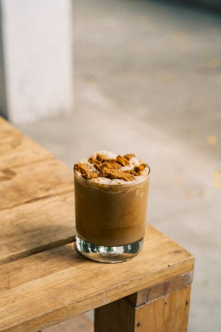 Delicious iced coffee glass topped with crunchy biscuits on a rustic wooden table.