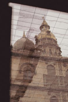 A historic cathedral with domes is captured through a rain-soaked window, reflecting its grandeur.