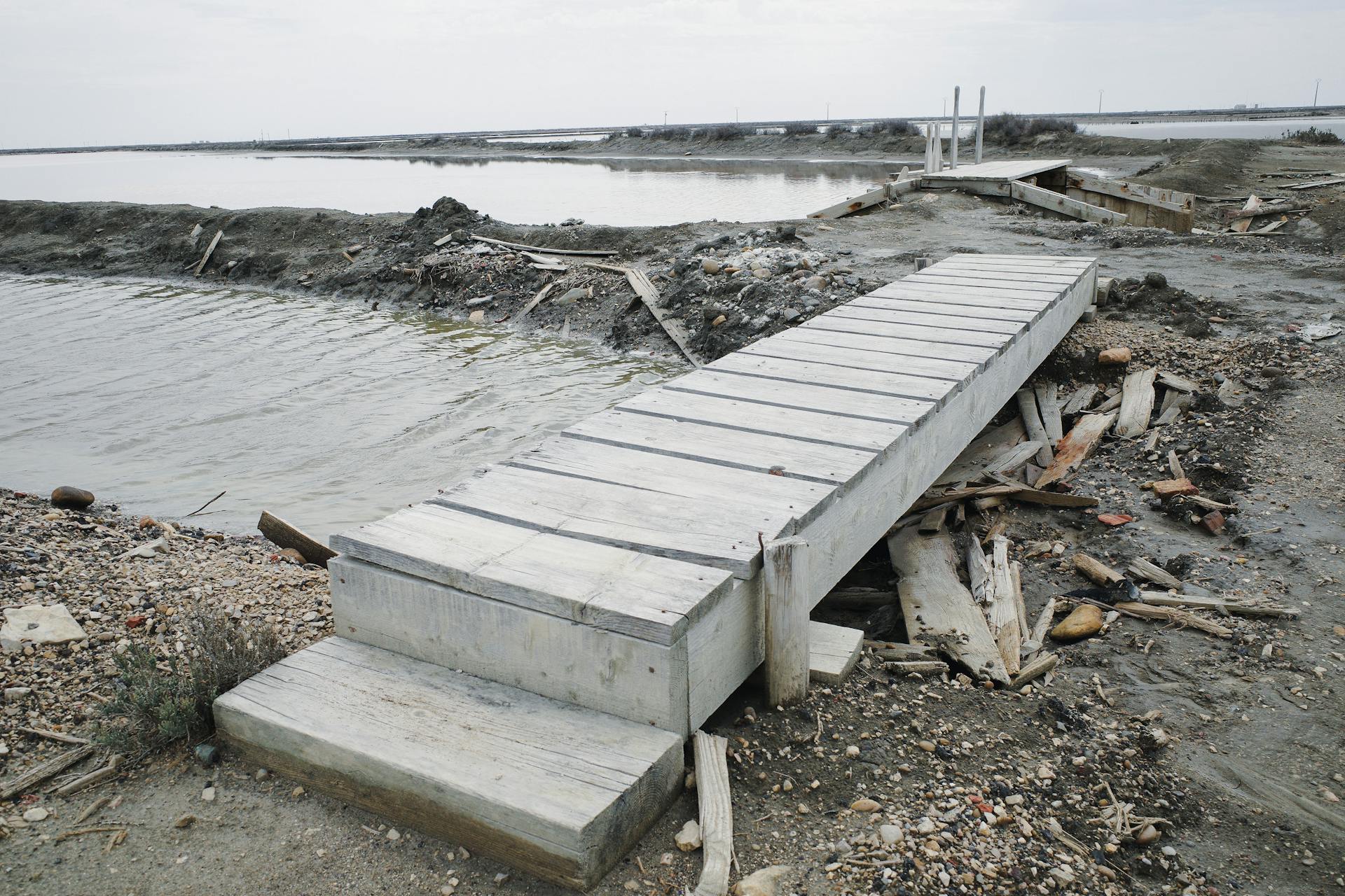 A deserted wooden bridge lying over a rugged riverside landscape.