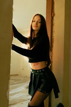 A young woman in fashionable attire posing with soft lighting indoors. Artistic portrait with warm tones.