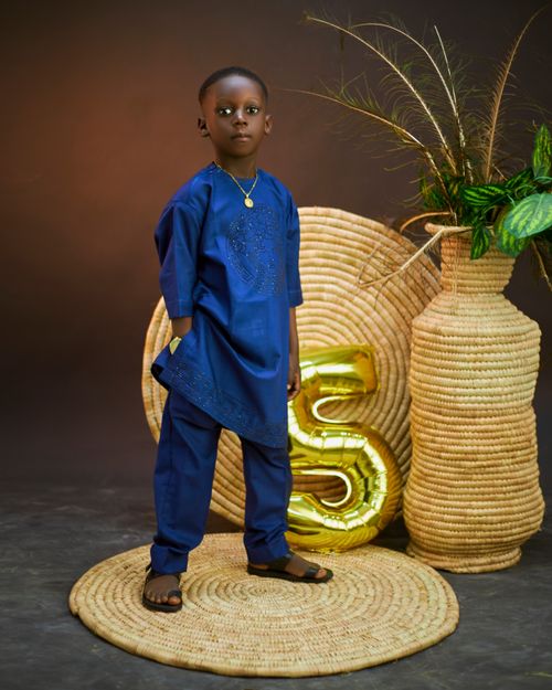 Free Child in blue traditional attire standing by decorative elements and a '5' balloon. Stock Photo