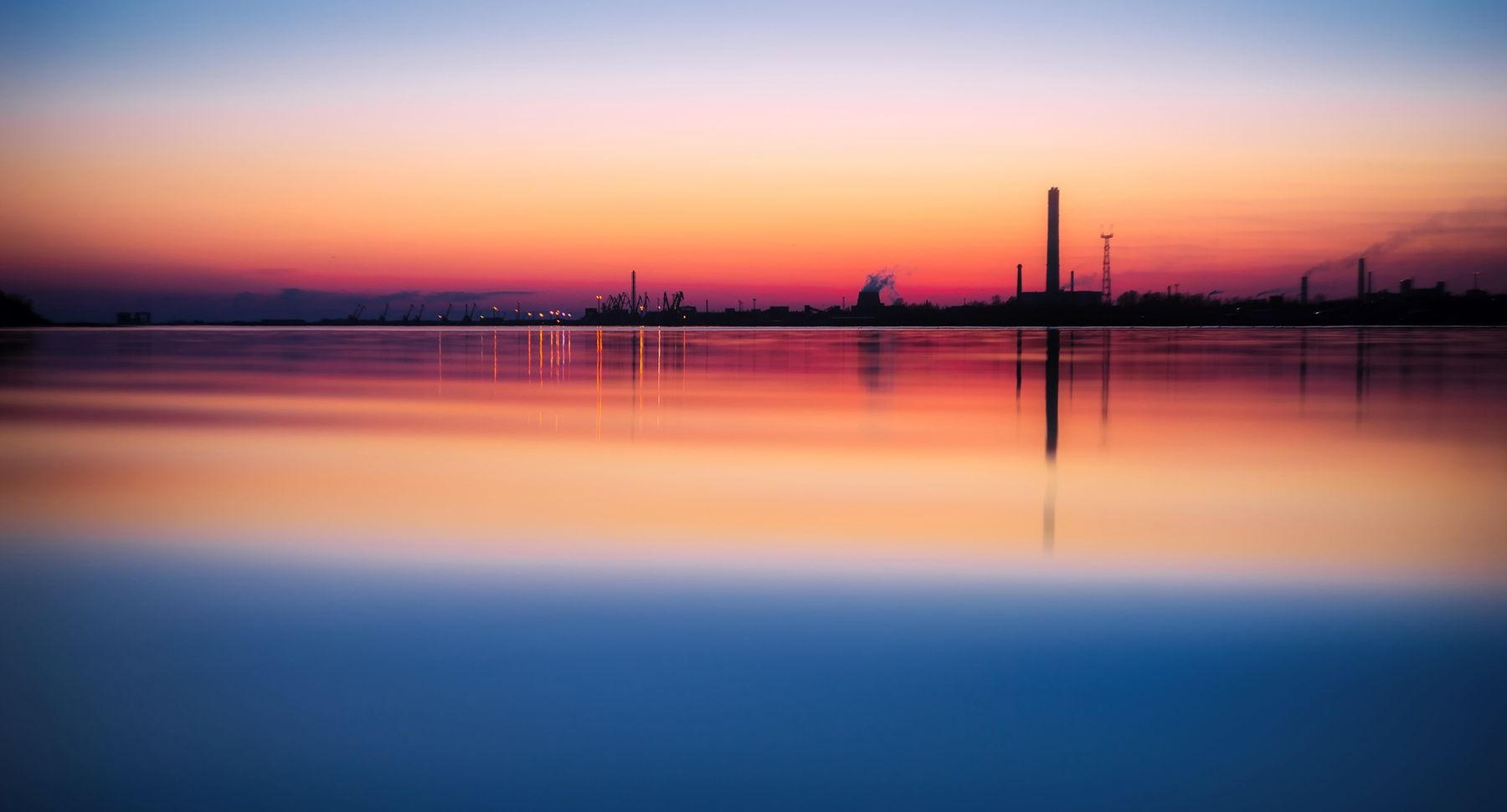 Industrial skyline reflected in still water at sunset, photo by Pixabay on Pexels