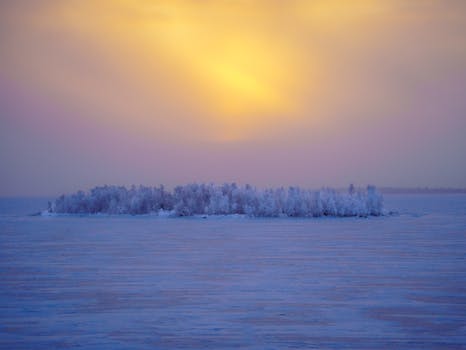 A serene view of a snowy island under a vibrant sunset in Kemi, Lapland, Finland.