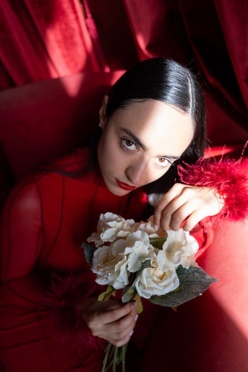 Free Portrait of a woman in a red dress holding white roses in dramatic lighting. Stock Photo