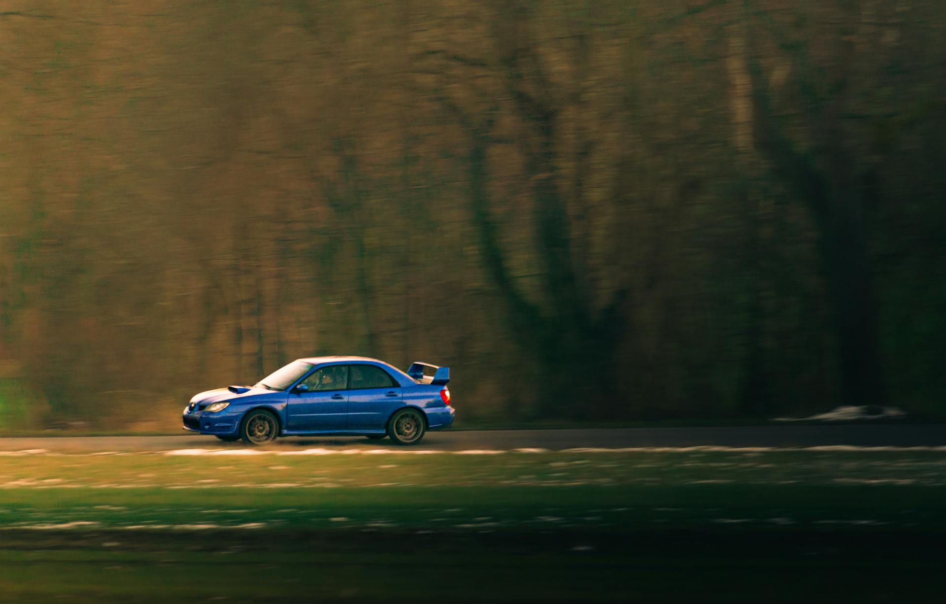 A vibrant blue car zooms along a scenic road, capturing speed and motion.