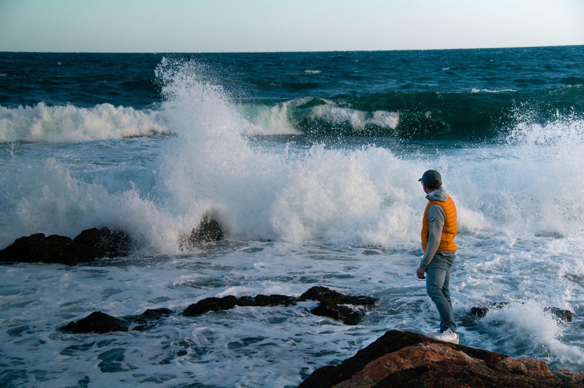 A man stands on rocks watching waves crash in Saint-Tropez, France coastline.
